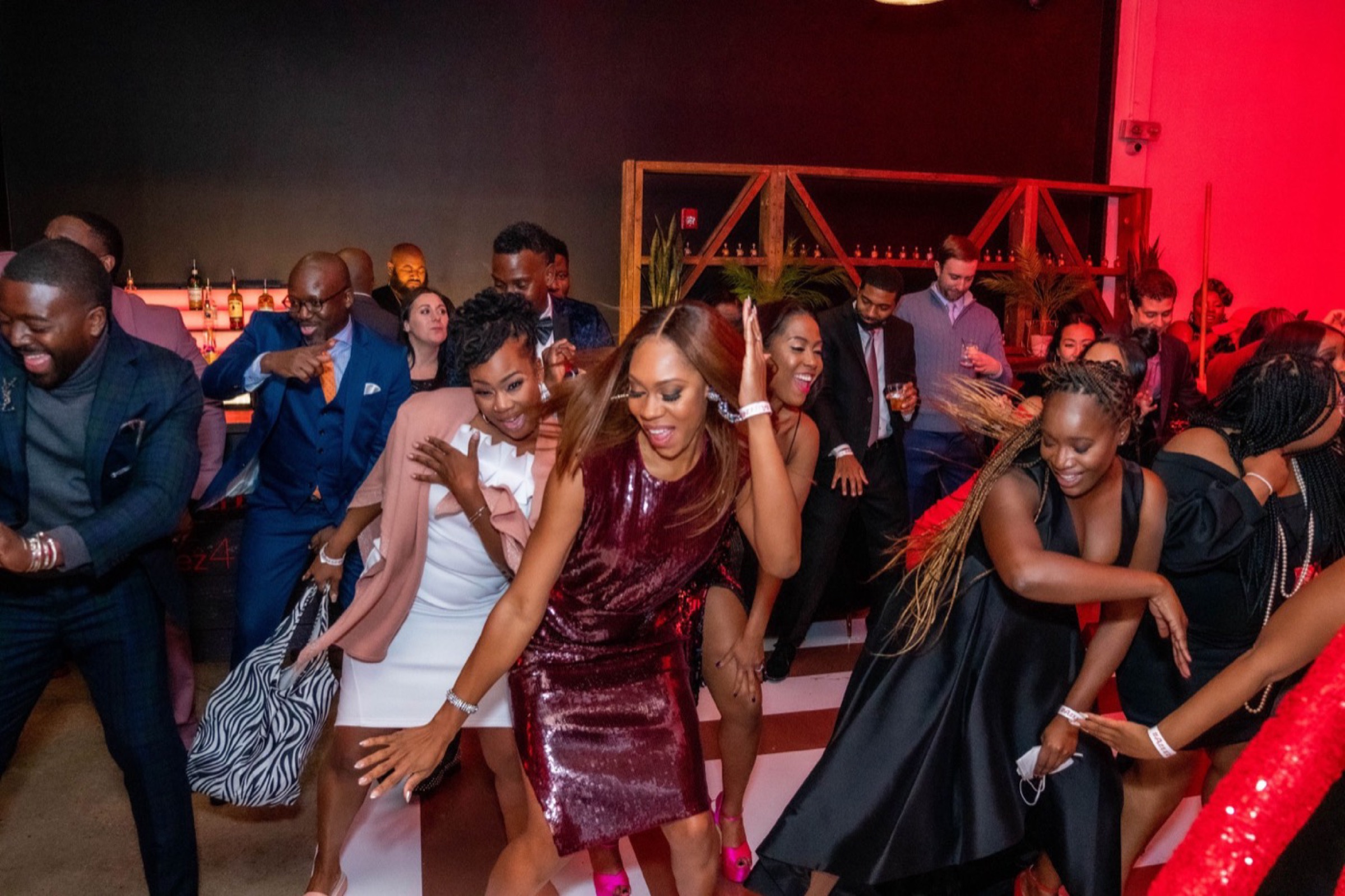 Guests in evening dress dancing together and laughing on a reception dance floor.